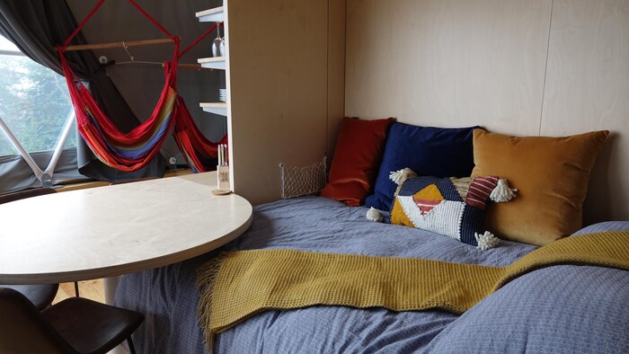 Un lit avec des coussins de couleur avec une table à côté et des hamacs à l'arrière.