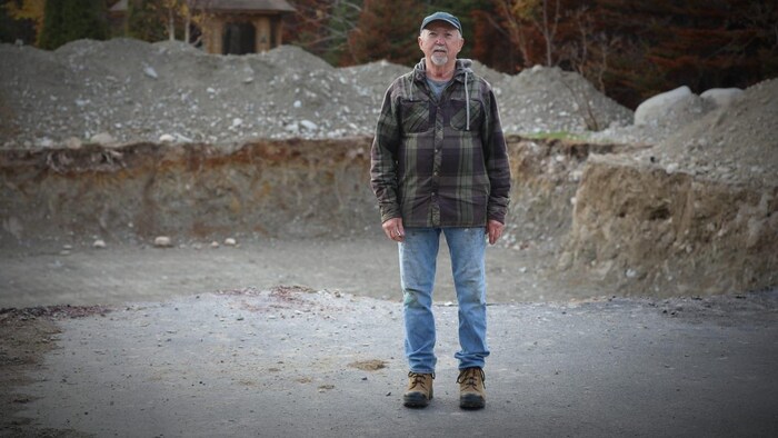 Un homme portant des jeans et une chemise à carreaux est debout dans un expansive  trou, entouré de sable et de roches.