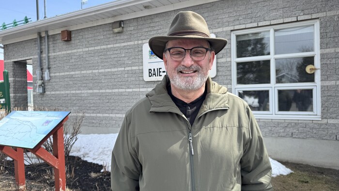 Gérald Beaulieu, préfet de la Matanie et maire de Baie-des-sables, porte un chapeau et des lunettes, devant l'hotel de Ville de Baie-des-Sables.