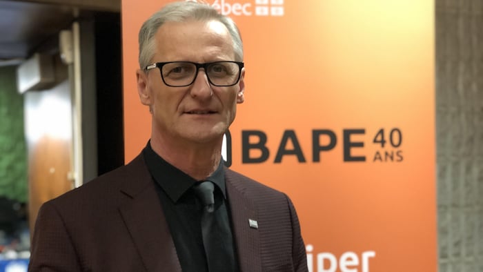 Gérald Savard devant une affiche du BAPE.