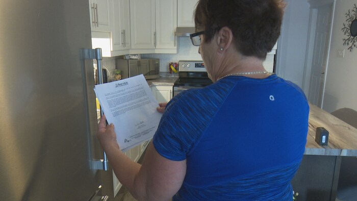 Une femme dans sa cuisine avec un document dans les mains.