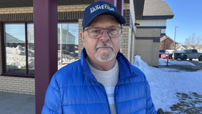 Un homme sourit à la caméra, un bâtiment derrière lui.