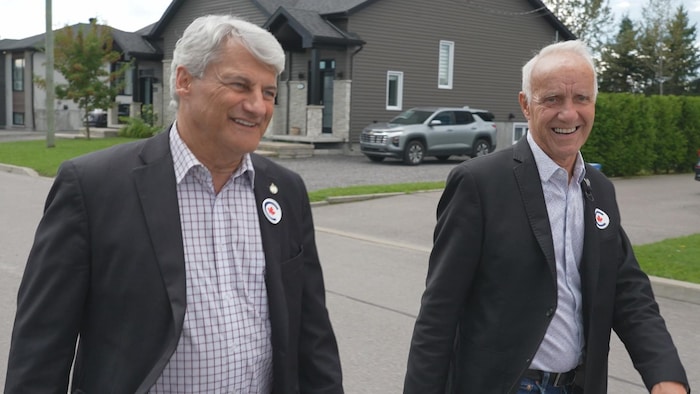 Gérard Deltell et Régis Gaudreault marchent dans une rue résidentielle.