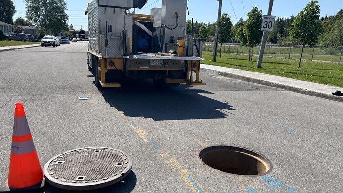 Une bouche d'égouts ouverte dans la rue derrière un camion.