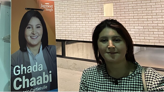 Une femme debout devant une pancarte électorale.