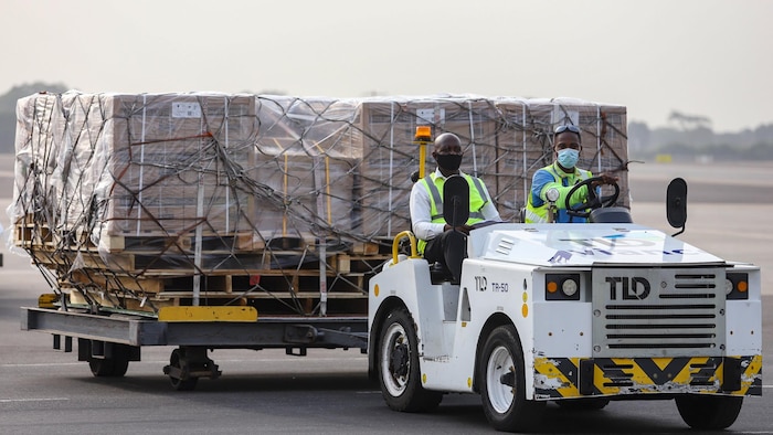 Deux hommes transportent des boîtes de doses de vaccins à bord d'un véhicule sur le tarmac de l'aéroport d'Accra. 