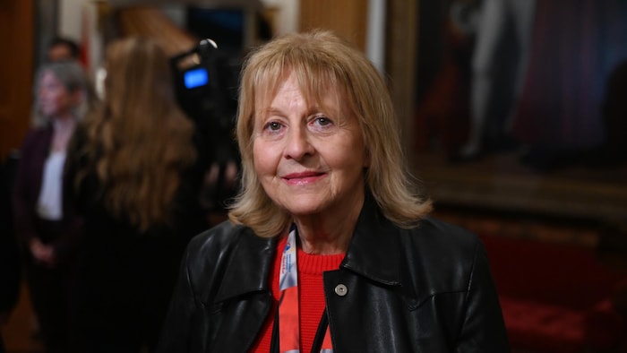 Ghislaine Foulem à l'Assemblée législative. En arrière-plan il y a des journalistes qui posent des questions à la première ministre.  