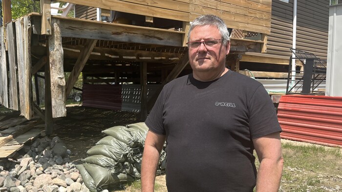 Un homme devant un chalet et des sacs de sable.