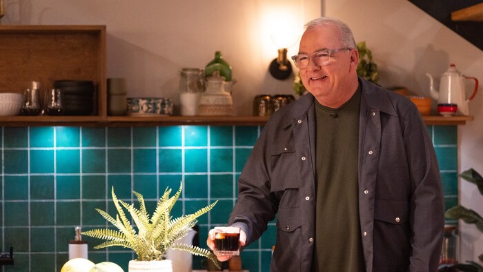 Gildor Roy souriant, avec un verre à la main, sur le plateau de télévision.