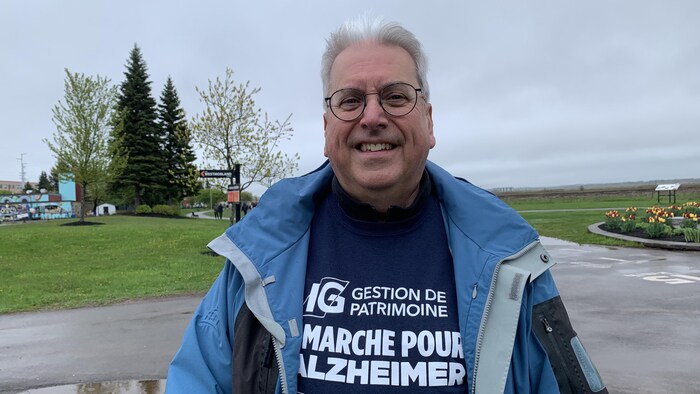 Un homme souriant dehors sous la pluie porte un chandail de la marche pour l'Alzheimer. 