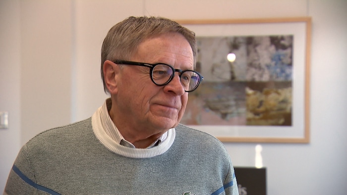 Un homme sourit devant une toile dans un bureau blanc.
