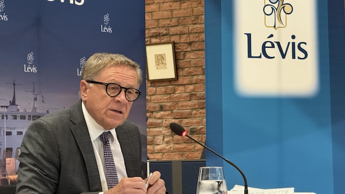 Gilles Lehouillier assis à une table derrière un micro.