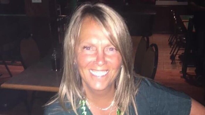 Une femme souriante avec un chandail vert et un collier vert au cou.