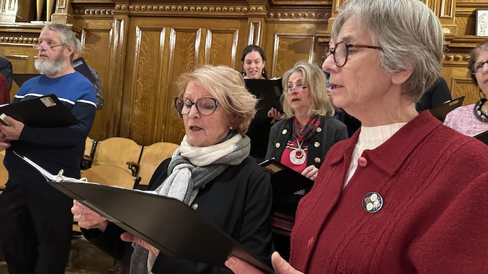 Deux femmes chantent en avant-plan avec d'autres choristes derrière.