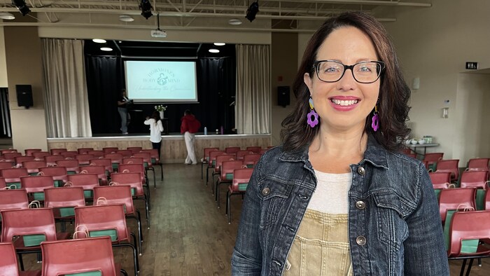 Une femme vêtue d'une veste en jeans pose pour une photo le dos à une rangée de chaises rouges.
