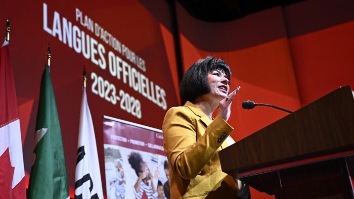 Ginette Petitpas Taylor prononce une allocution sur un fond rouge. Les mots « Plan d'action pour les langues officielles 2023-2028 » sont écrits derrière elle sur le mur.