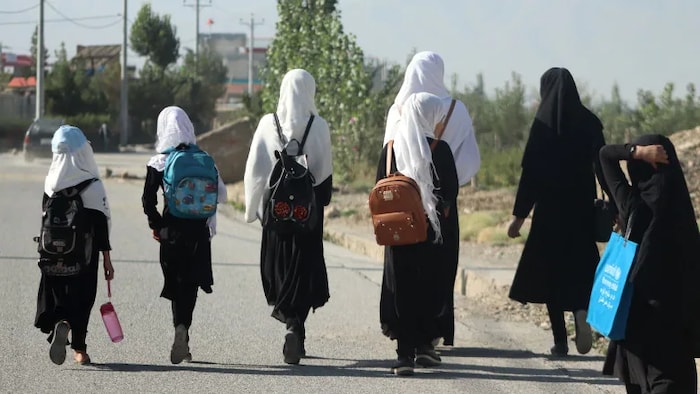 De jeunes filles, munies de sacs à dos, marchent sur une route.