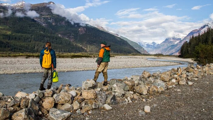 Deux personnes sont debout près d'une rivière et regardent des montagnes au loin.