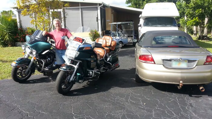 Glenn McGill debout entre deux motos, dont une à vendre, dans son entrée à côté d'autres véhicules.