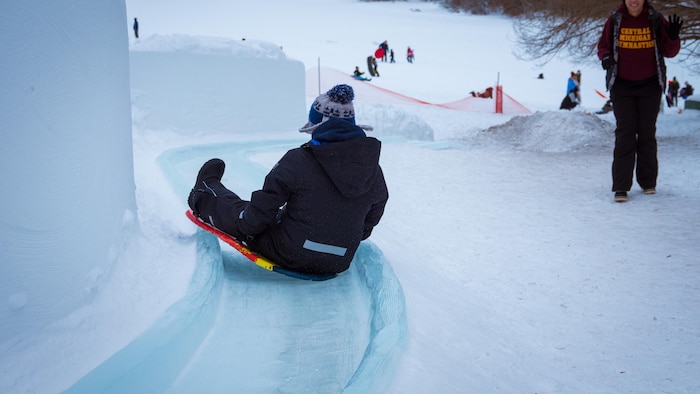 Un enfant descend la glissade de glace sur une planche.