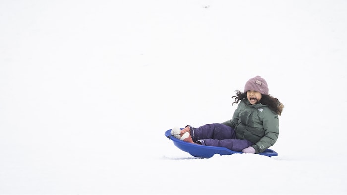 Une petite fille fait du toboggan sur une pente enneigée.