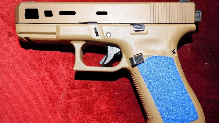 Un pistolet brun couché sur le côté sur fond rouge.
