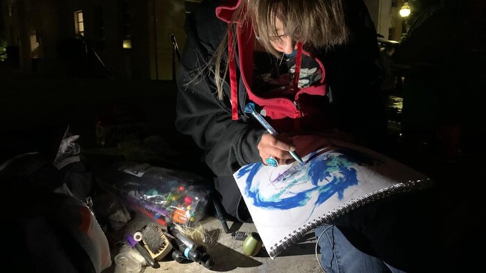 A woman, sitting outside at night, is drawing.