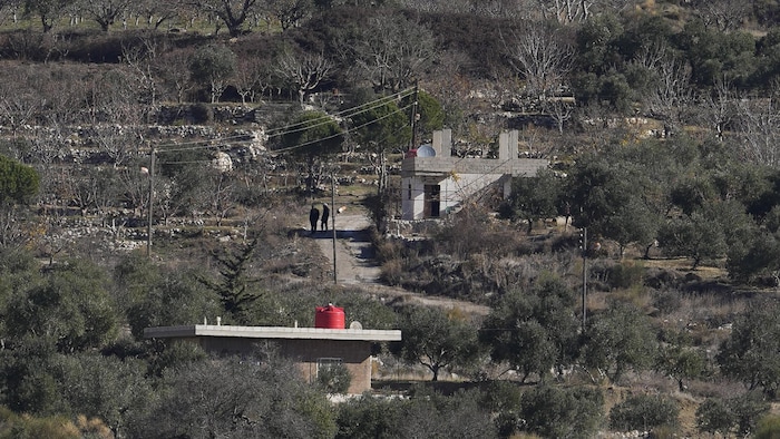 Deux personnes marchent sur une route près d'une maison et entouré de végétation, le 15 décembre 2024. 