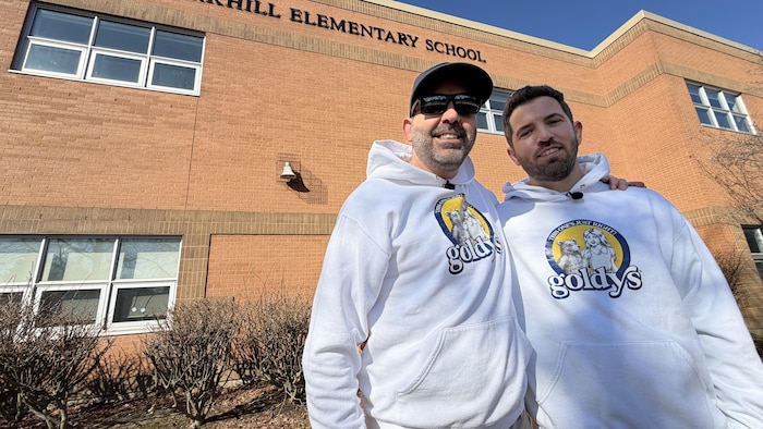 Deux hommes se tiennent debout devant la façade d'une école.