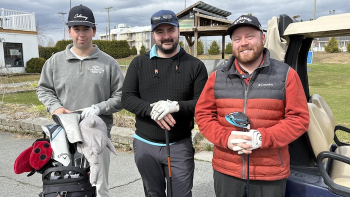 Trois golfeurs, mains sur leurs bâtons, prennent la pose en souriant.