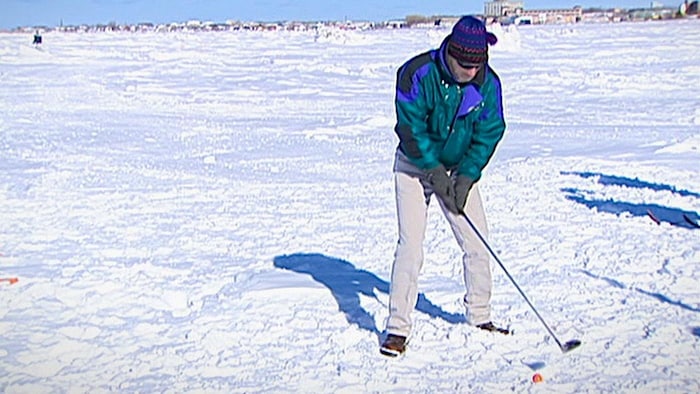 Un golfeur s'apprête à frapper une balle dans la neige, sur la banquise, en face du centre-ville de Rimouski.