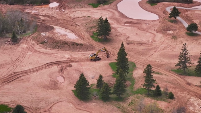 Une pelleteuse fait des travaux pour aménager un terrain de golfe. 
