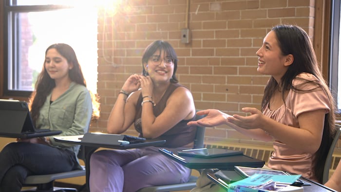 Trois étudiantes d'un groupe sourient en discutant d'un livre qu'elles ont lu.