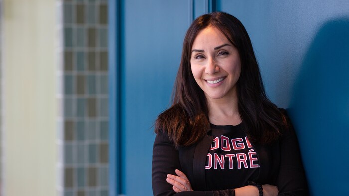Une femme souriante portant un chandail à l'effigie de Google Montréal prend la pose, les bras croisés.