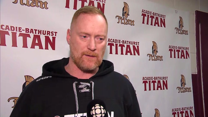 Gordie Dwyer devant un paravent décoré du logo du Titan d'Acadie-Bathurst.
