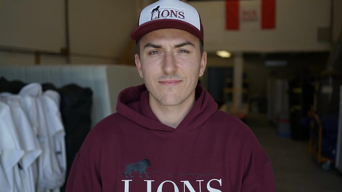 Un homme qui porte un chandail et une casquette qui arborent le nom de son entreprise, Lions.