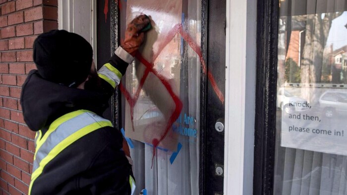 Un homme efface une croix gammée rouge peinte sur une porte.