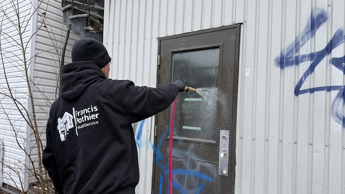 Un homme nettoie des graffitis sur une porte extérieure.
