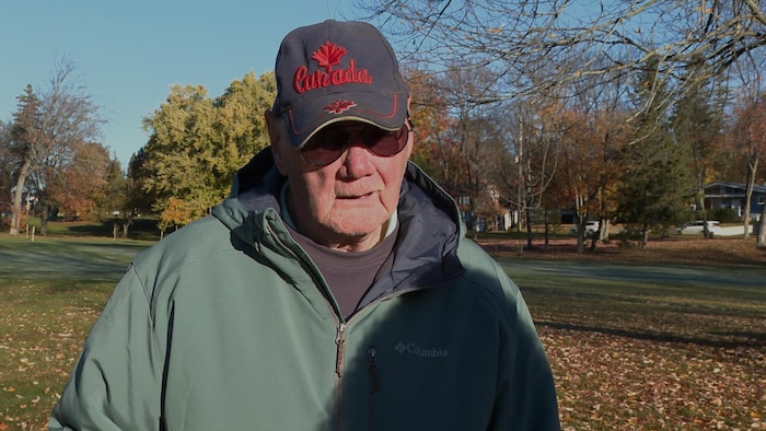 Un homme portant une casquette avec écrit Canada et un manteau à capuchon en entrevue dans un parc.