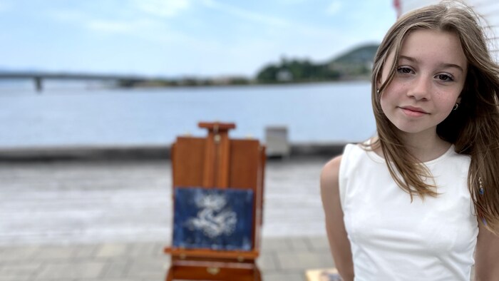 Une jeune peintre et sa toile en arrière plan.