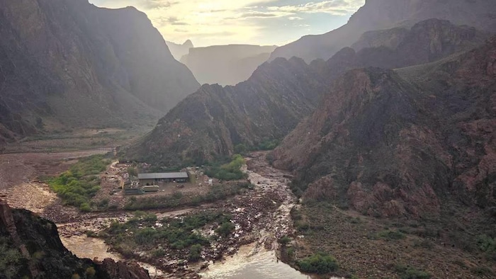 Une vallée est inondée par une eau boueuse. Un bâtiment logé au creux d'un canyon semble épargné.