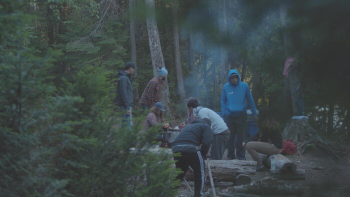 Des adolescents en forêt cuisinent autour d'un feu de camp.