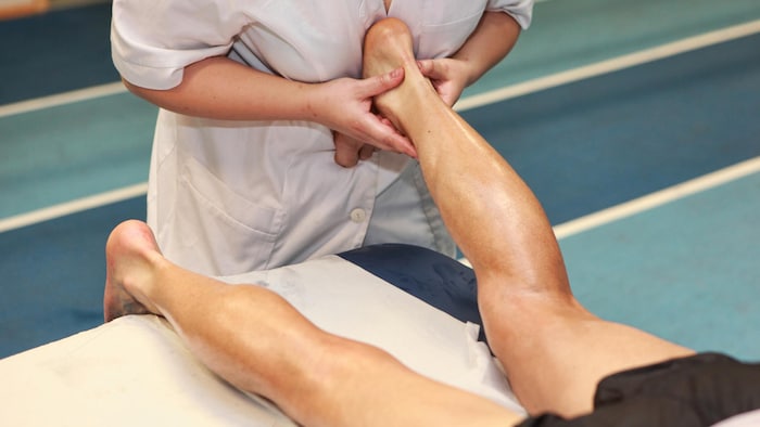Une thérapeute masse le tendon d'Achille d'un patient couché sur le ventre.