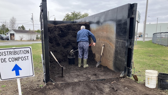 Un homme à l'intérieur d'un conteneur met du compost dans une chaudière à l'aide d'une pelle.