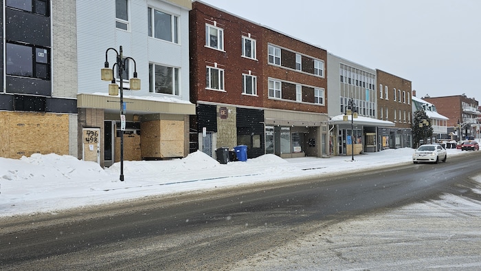 Une rue enneigée avec des commerces dont certains ont des vitrines placardées.