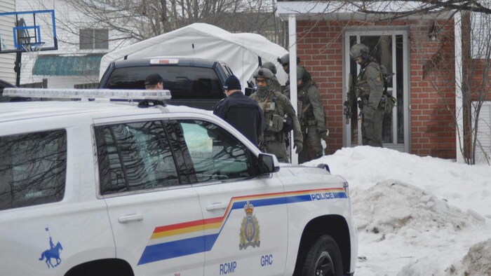 Photo de policiers en uniforme tactique qui sortent d'une résidence; un véhicule de la GRC est garé à proximité.