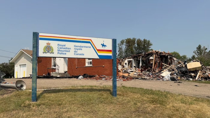 Une affiche de la GRC devant un bâtiment ravagé par les flammes.