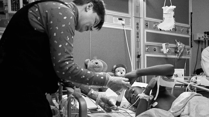 Un médecin rend visite à un enfant couché dans lad   lit d'hôpital. 