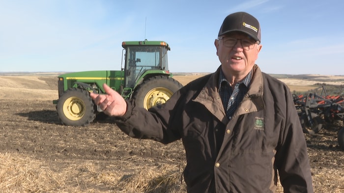 Greg Hawkwood, dans son champ, parle, un tracteur derrière lui.