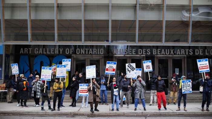 Des employés sur le piquet de grève avec des pancartes devant le musée.